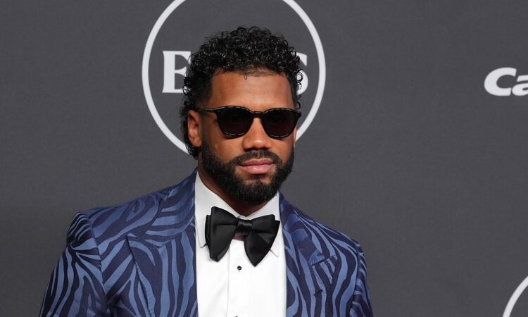 Russell Wilson poses in a patterned blue tuxedo jacket and sunglasses on the ESPY Awards red carpet.