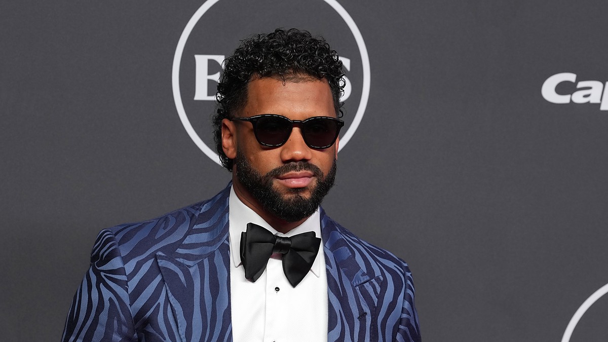 Russell Wilson poses in a patterned blue tuxedo jacket and sunglasses on the ESPY Awards red carpet.