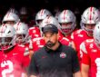 Ohio State head coach Ryan Day walks out of the tunnel with helmeted players behind and beside him.