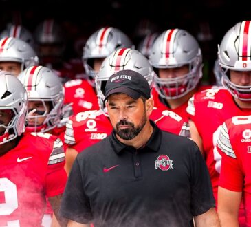Ohio State head coach Ryan Day walks out of the tunnel with helmeted players behind and beside him.