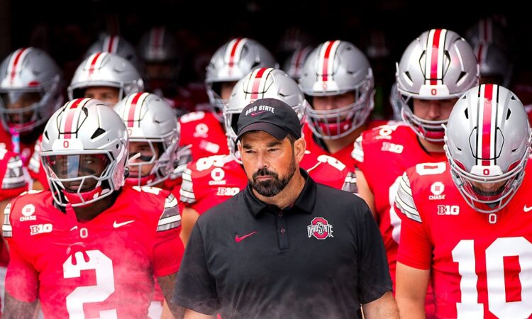 Ohio State head coach Ryan Day walks out of the tunnel with helmeted players behind and beside him.