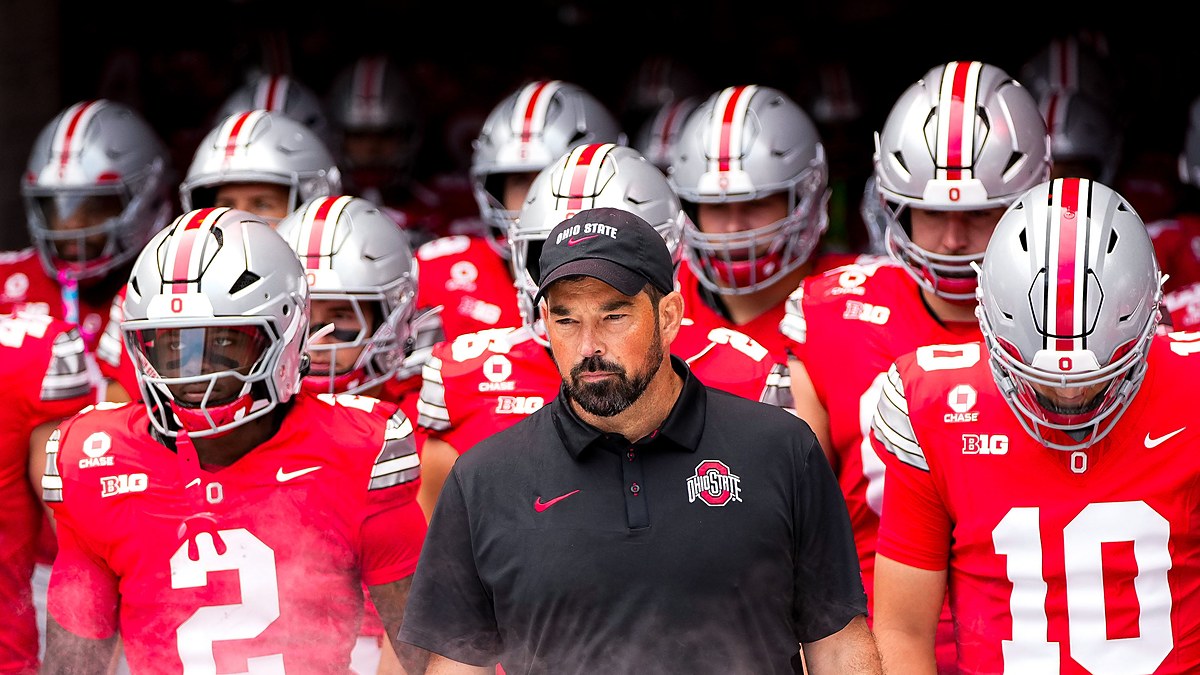 Ohio State head coach Ryan Day walks out of the tunnel with helmeted players behind and beside him.