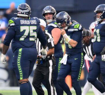 Seattle Seahawks quarterback Sam Darnold reaches for his facemask among teammates after being sacked.