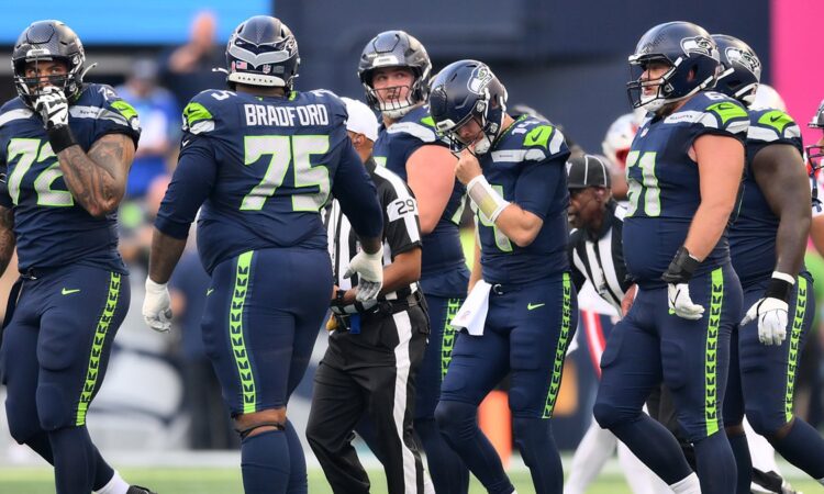 Seattle Seahawks quarterback Sam Darnold reaches for his facemask among teammates after being sacked.