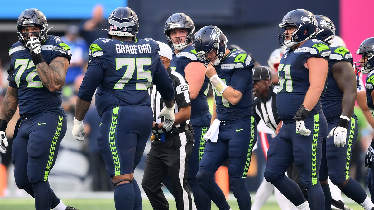 Seattle Seahawks quarterback Sam Darnold reaches for his facemask among teammates after being sacked.