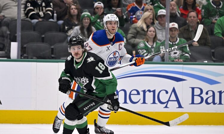 Stars center Sam Steel and Oilers center Connor McDavid skate side by side as both look up for the puck.