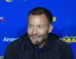 Los Angeles Rams head coach Sean McVay smiles while speaking into a microphone in front of a Rams backdrop.