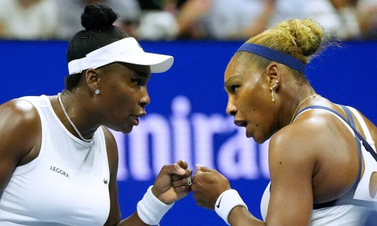 Venus Williams and Serena Williams bump fists and talk face to face between points during a doubles match.
