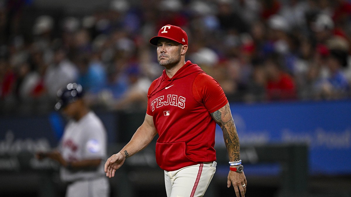 Texas Rangers manager Skip Schumaker walks across the infield in a red Tejas hooded top.
