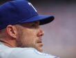 Texas Rangers manager Skip Schumaker looks out from the dugout in a road gray uniform.