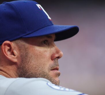 Texas Rangers manager Skip Schumaker looks out from the dugout in a road gray uniform.