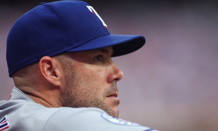 Texas Rangers manager Skip Schumaker looks out from the dugout in a road gray uniform.