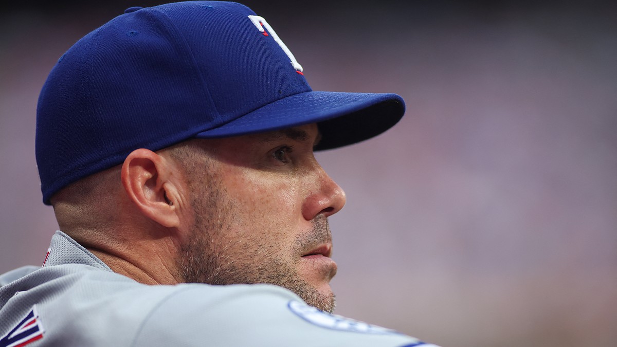 Texas Rangers manager Skip Schumaker looks out from the dugout in a road gray uniform.