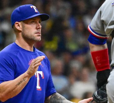 Texas Rangers manager Skip Schumaker raises a hand to signal for a relief pitcher as his catcher waits.