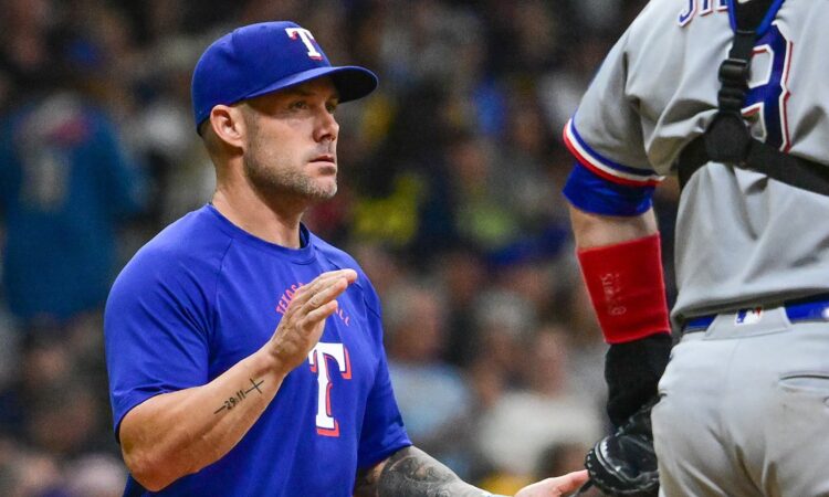 Texas Rangers manager Skip Schumaker raises a hand to signal for a relief pitcher as his catcher waits.