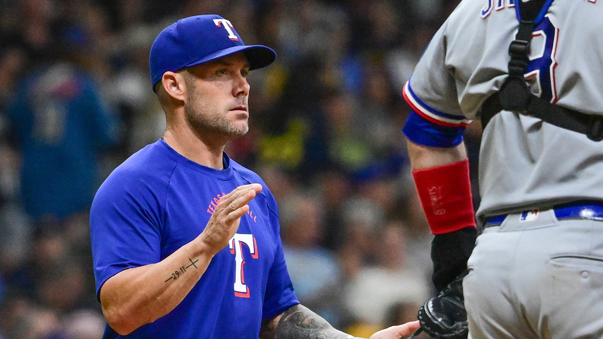 Texas Rangers manager Skip Schumaker raises a hand to signal for a relief pitcher as his catcher waits.