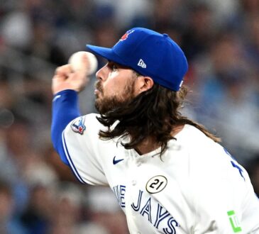 Toronto Blue Jays relief pitcher Spencer Arrighetti, his long hair flowing from under his cap, delivers a pitch.