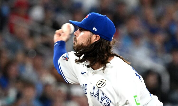 Toronto Blue Jays relief pitcher Spencer Arrighetti, his long hair flowing from under his cap, delivers a pitch.