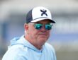 Cowboys chief operating officer Stephen Jones watches training camp in sunglasses, a ball cap, and a light blue hoodie.