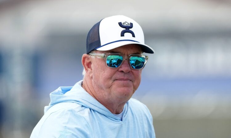 Cowboys chief operating officer Stephen Jones watches training camp in sunglasses, a ball cap, and a light blue hoodie.