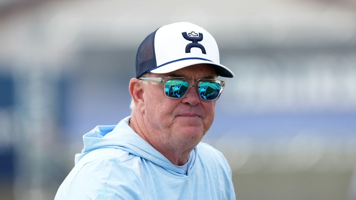 Cowboys chief operating officer Stephen Jones watches training camp in sunglasses, a ball cap, and a light blue hoodie.