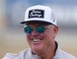 Cowboys chief operating officer Stephen Jones smiles at training camp in a ball cap and sunglasses.