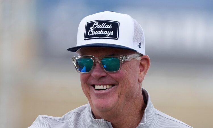 Cowboys chief operating officer Stephen Jones smiles at training camp in a ball cap and sunglasses.