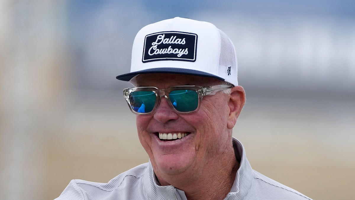 Cowboys chief operating officer Stephen Jones smiles at training camp in a ball cap and sunglasses.