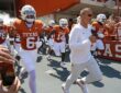 Texas Longhorns head coach Steve Sarkisian leads his players onto the field as fans cheer from the stands.
