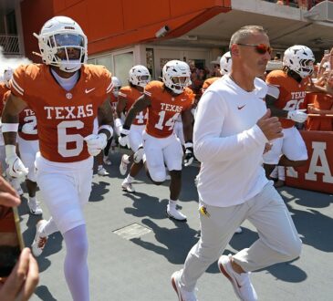 Texas Longhorns head coach Steve Sarkisian leads his players onto the field as fans cheer from the stands.