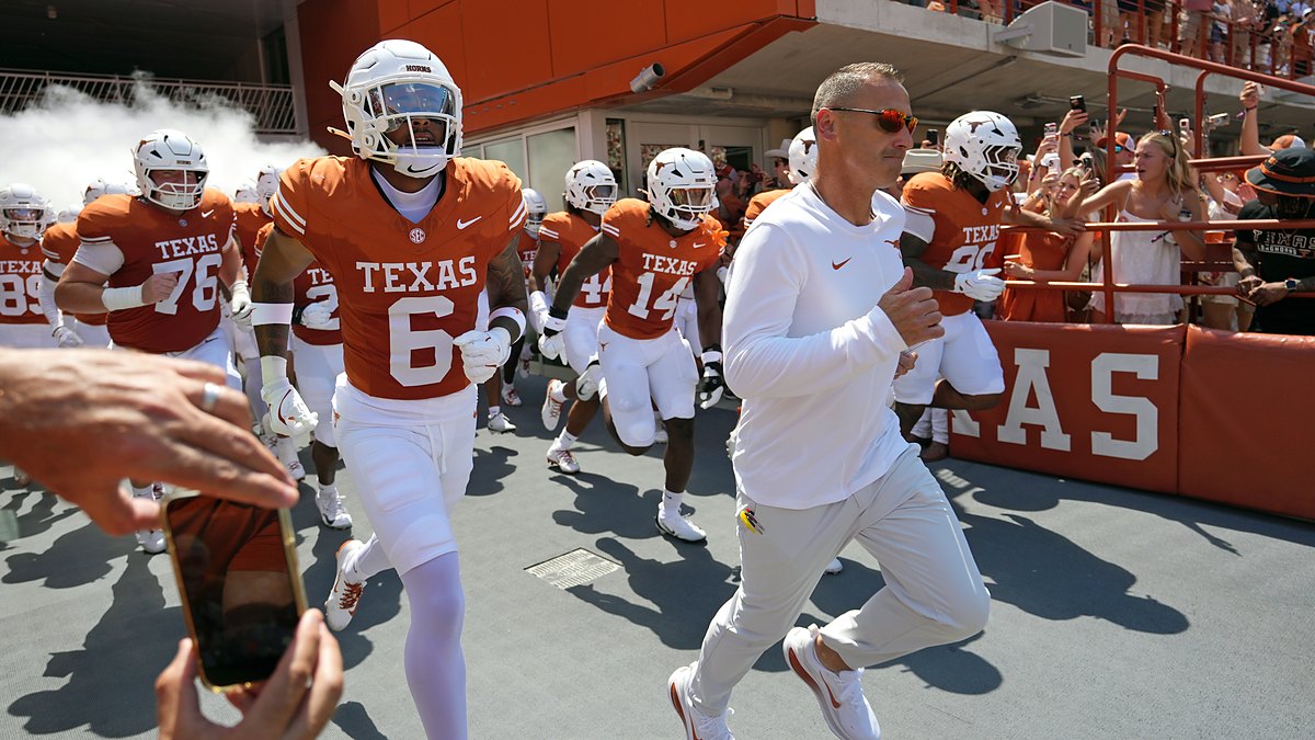 Texas Longhorns head coach Steve Sarkisian leads his players onto the field as fans cheer from the stands.