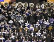 TCU Horned Frogs marching band members in rain gear play sousaphones, drums, and cymbals in the stands.
