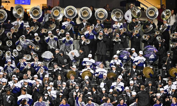 TCU Horned Frogs marching band members in rain gear play sousaphones, drums, and cymbals in the stands.