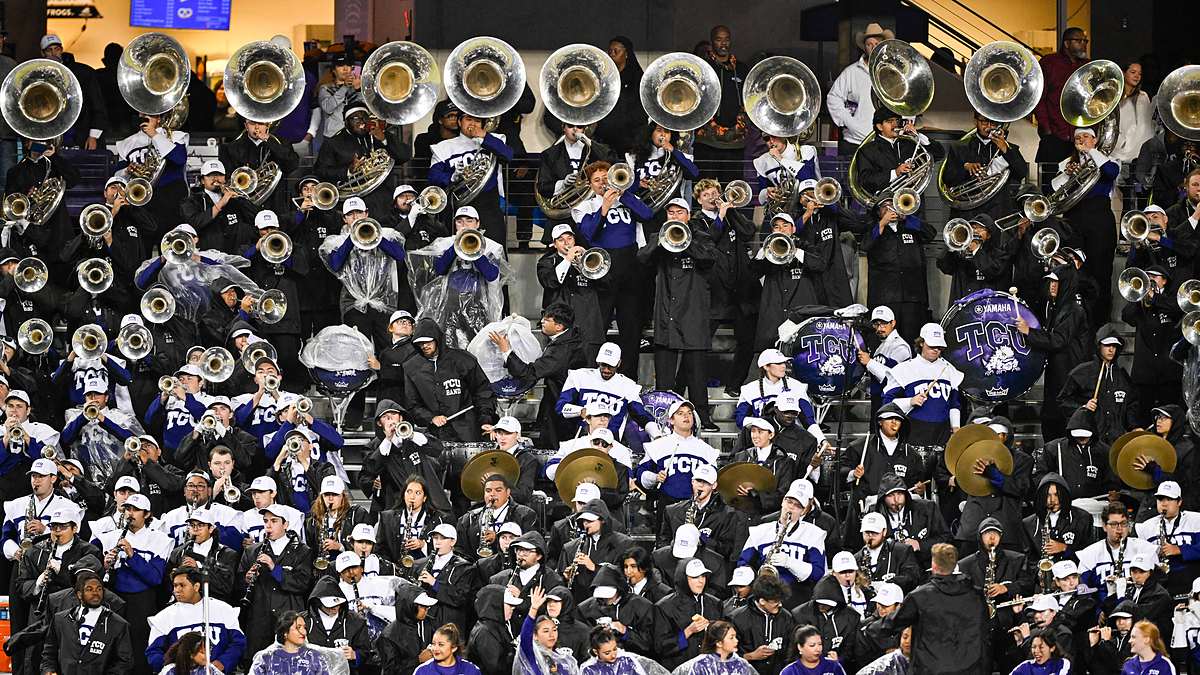 TCU Horned Frogs marching band members in rain gear play sousaphones, drums, and cymbals in the stands.