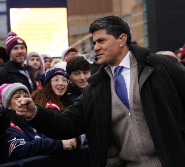 Former New England Patriot Tedy Bruschi bumps fists with fans along a barricade before a playoff game.