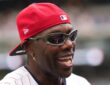 Former NFL receiver Terrell Owens smiles in a red cap and pinstripes during All-Star week.