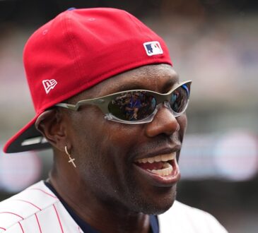 Former NFL receiver Terrell Owens smiles in a red cap and pinstripes during All-Star week.