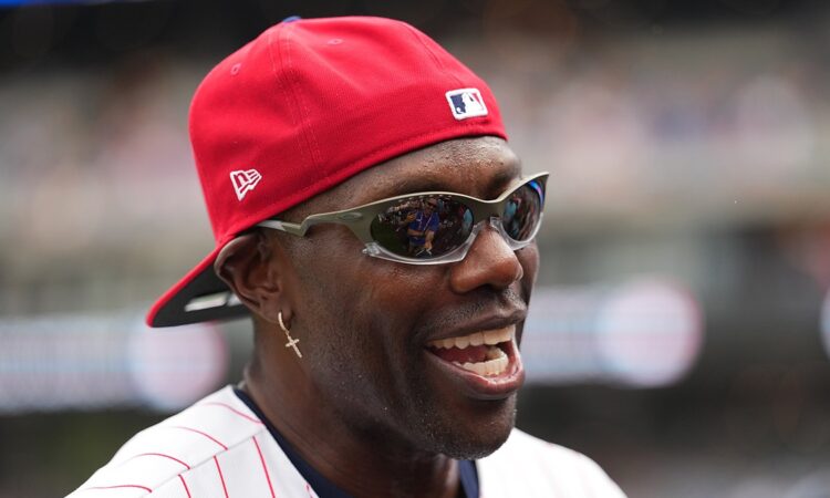 Former NFL receiver Terrell Owens smiles in a red cap and pinstripes during All-Star week.