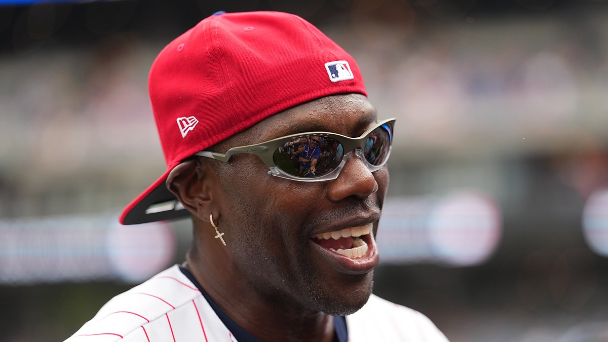 Former NFL receiver Terrell Owens smiles in a red cap and pinstripes during All-Star week.
