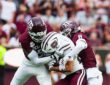 Two Texas A&M defenders wrap up a Missouri State ball carrier who holds the ball against his chest.