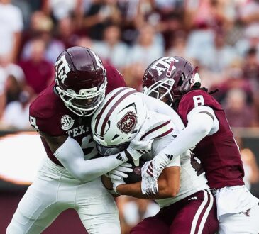Two Texas A&M defenders wrap up a Missouri State ball carrier who holds the ball against his chest.