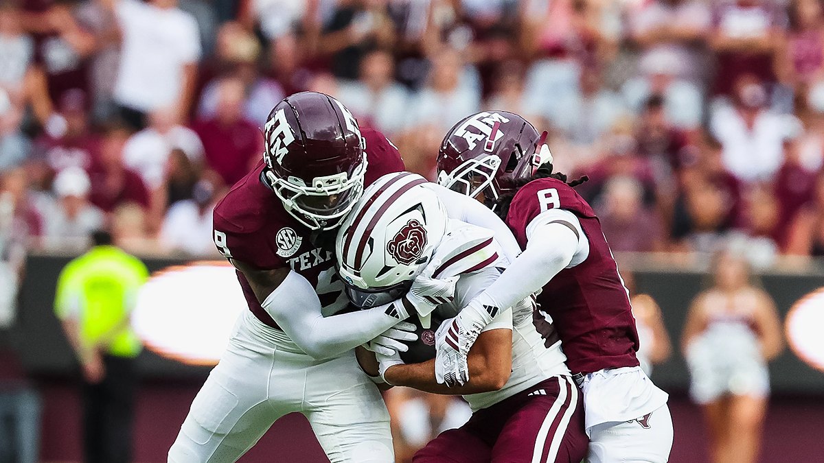 Two Texas A&M defenders wrap up a Missouri State ball carrier who holds the ball against his chest.