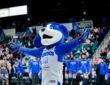 Texas Legends mascot Dunker spreads his arms on the court as players in warmup shirts stand behind him.