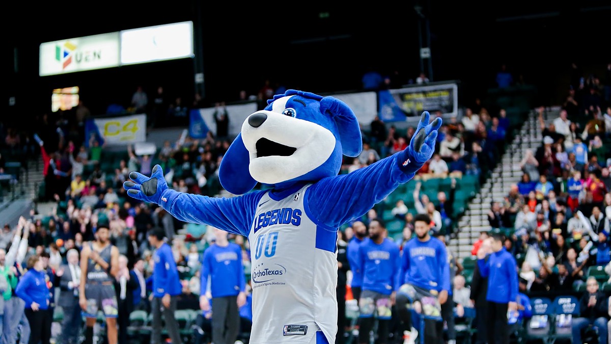 Texas Legends mascot Dunker spreads his arms on the court as players in warmup shirts stand behind him.