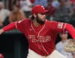 Texas Rangers pitcher Trevor Williams, in a red Tejas jersey, rears back to throw a pitch from the mound.