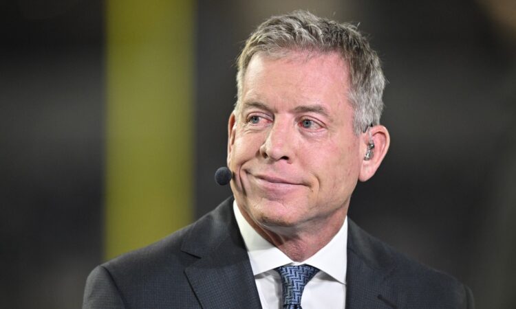Television commentator Troy Aikman speaks on camera in a suit and earpiece before the Cowboys and Cardinals game.