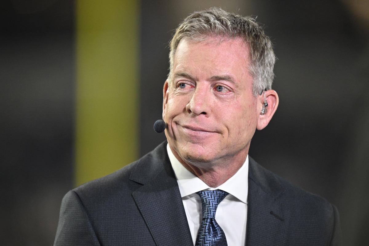 Television commentator Troy Aikman speaks on camera in a suit and earpiece before the Cowboys and Cardinals game.