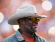 Former Texas Longhorns quarterback Vince Young smiles in a cowboy hat and sunglasses on the field during a game.