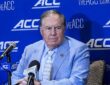 North Carolina head coach William Belichick sits at a table with microphones in front of an ACC backdrop.