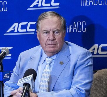 North Carolina head coach William Belichick sits at a table with microphones in front of an ACC backdrop.